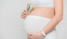 Cropped view of pregnant woman holding dollar banknotes and touching belly on grey background, concept of surrogacy maternity Cropped view of pregnant woman holding dollar banknotes and touching belly on grey background, concept of surrogacy maternity