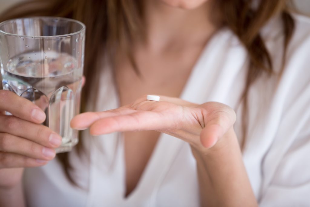 Woman holding pill and glass of water, close up view Woman holding pill and glass of water in hands taking emergency medicine, supplements or antibiotic antidepressant painkiller medication to relieve pain, meds side effects concept, close up view