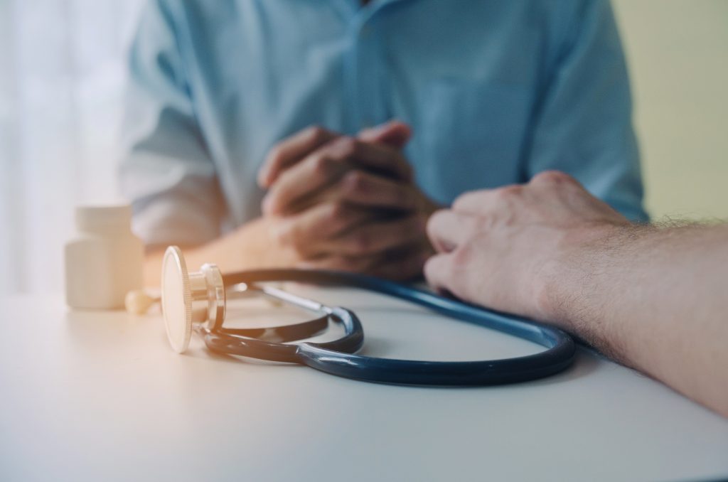 close up of hand of doctor and suffering patient sitting with stethoscope and bottle of pills on desk in hospital, encouragement, health care, medical, medicine, pharmacy and insurance concept close up of hand of doctor and suffering patient sitting with stethoscope and bottle of pills on desk in hospital, encouragement, health care, medical, medicine, pharmacy and insurance concept