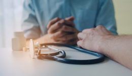 close up of hand of doctor and suffering patient sitting with stethoscope and bottle of pills on desk in hospital, encouragement, health care, medical, medicine, pharmacy and insurance concept