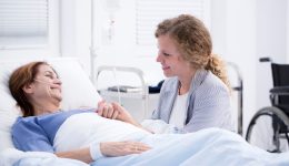 Young smiling woman kneeling by the bed visiting her happy mom recovering from illness in a hospital