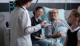 Elderly people care nurse reviewing files of senior male patient bedridden in geriatric hospital. Female general practitioner listening to older hospitalized man symptoms.