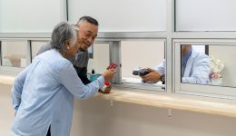 Adult mature couple stand in front of cashier counter of drug department paying with credit card to payment transaction machine at cashier counter in hospital. Pharmacist service or patient counseling