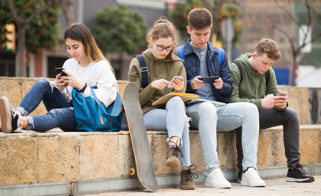 Group of teens using smartphones outdoors Teens using phones outdoors, concept of youth obsession with social networks