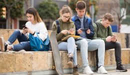 Teens using phones outdoors, concept of youth obsession with social networks